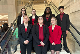  A group of students in business attire stand at the bottom of a flight of stairs